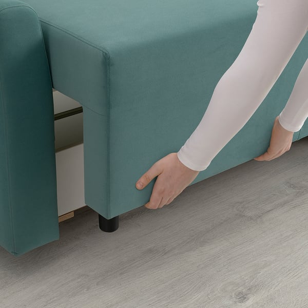 Person transforming green sofa-bed, revealing storage space beneath.