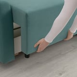 Person transforming green sofa-bed, revealing storage space beneath.
