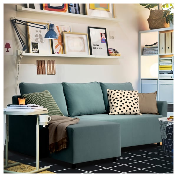 Modern living room with blue BRISSUND sectional sofa, colorful cushions, shelves with decor, and a cozy, inviting atmosphere.