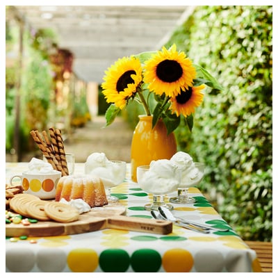 Yellow vase with sunflowers on green-yellow tablecloth. Dessert bowls, cookies, and cake.
