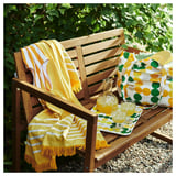 Bright yellow and green polka dot tray on wooden bench with lemonade, small glasses, and blankets.