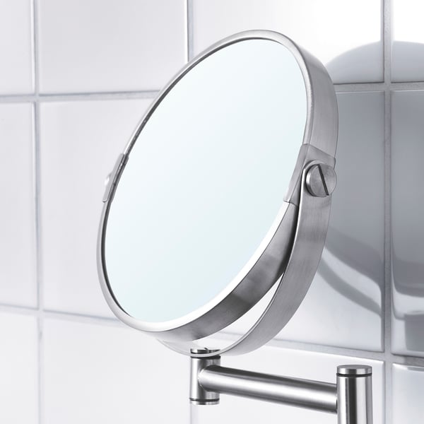 Round magnifying mirror with sleek metal frame mounted on wall, reflecting light and tiles, showcasing modern design.