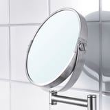 Round magnifying mirror with sleek metal frame mounted on wall, reflecting light and tiles, showcasing modern design.