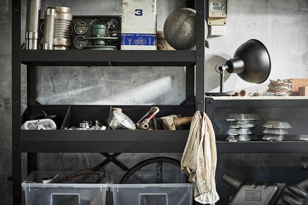 Black metal storage unit with various tools and containers on shelves. Includes a wall-mounted black lamp.