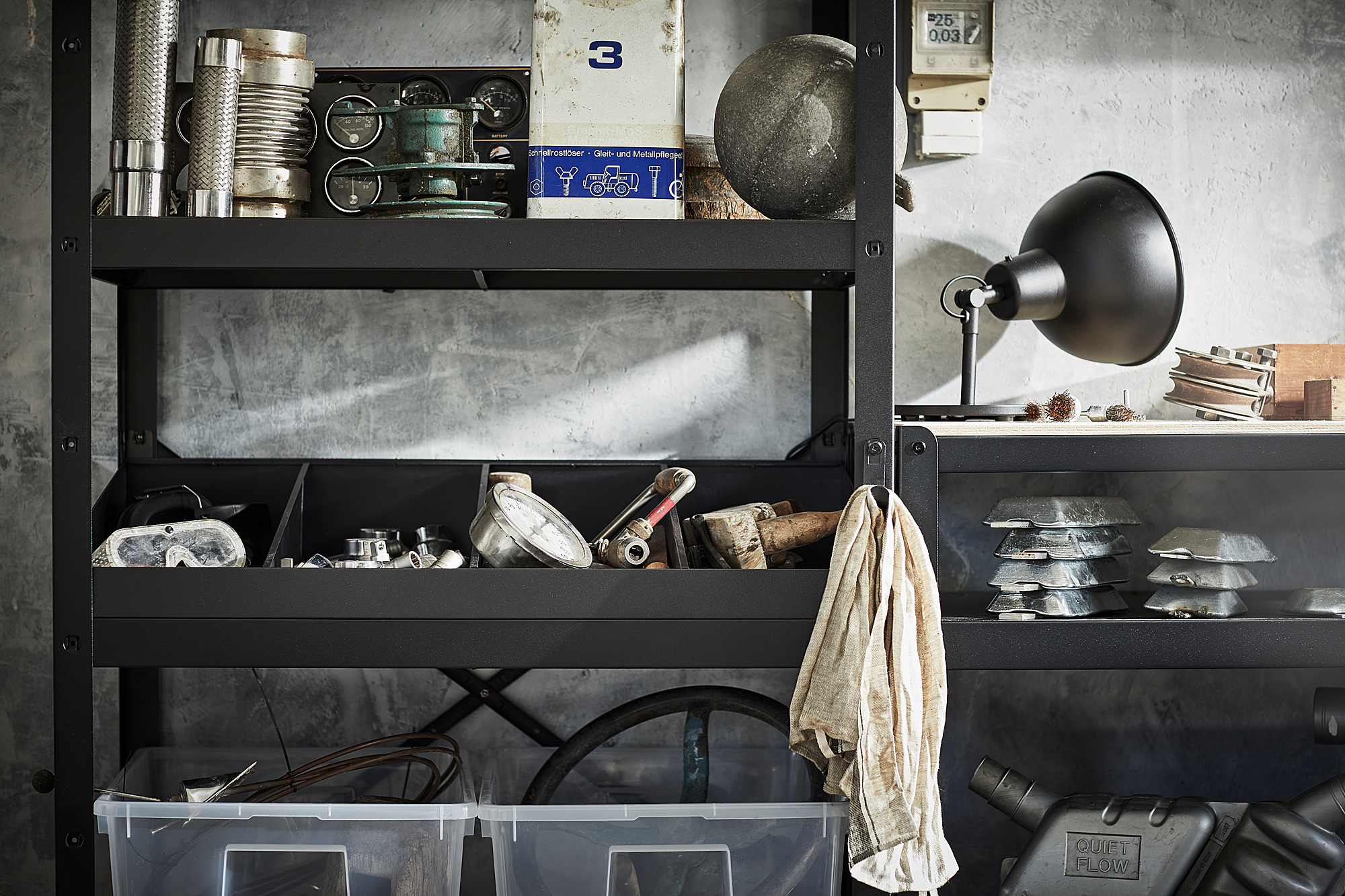 Black metal storage unit with various tools and containers on shelves. Includes a wall-mounted black lamp.