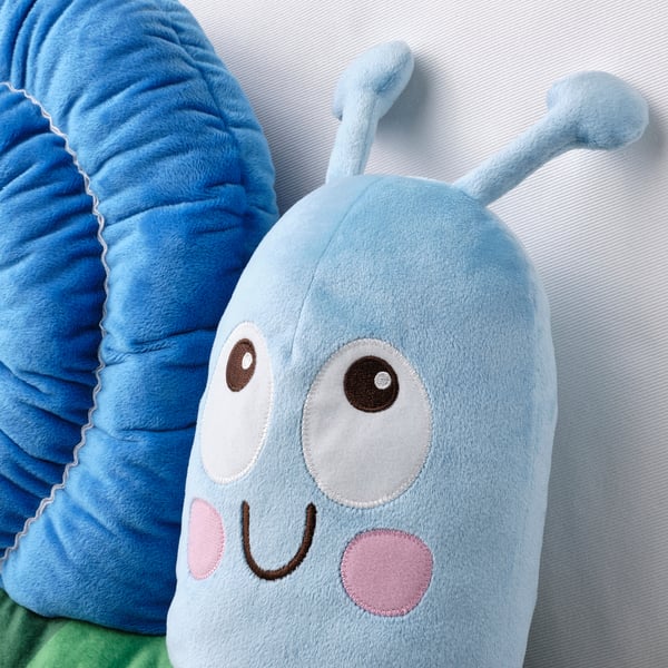 A plush, blue, snail-shaped pillow with large eyes and pink cheeks lies comfortably on a green surface.