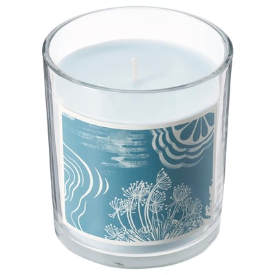 A BUKETTAPEL blue scented candle in a clear glass jar. It has a floral design and is cylindrical in shape.