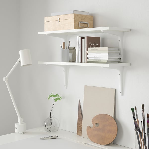 Two BURHULT shelves with books & art supplies. Desk with plant & lamp.