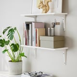 Wall-mounted white shelf holding books, a potted plant, and a box. BURHULT series, offering practical storage and display.