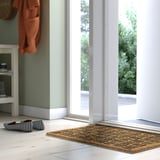 Cozy room with green walls, CYKELGRIND door mat at entrance, striped slippers, white floors, large window.
