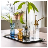 A set of three colorful, uniquely shaped glass vases on a tray, displaying plant cuttings in water.