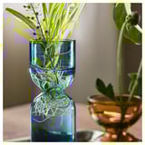 Glass vases holding plant cuttings, two blue and one brown, with water and roots visible.