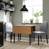DANDERYD dining set with extendable table, gray armchairs, black pendant light, and shelf with books and plants.
