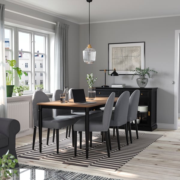 Modern dining room with DANDERYD 6-seat gray set. Table has wooden top, steel legs. Large window, plant, artwork, striped rug.