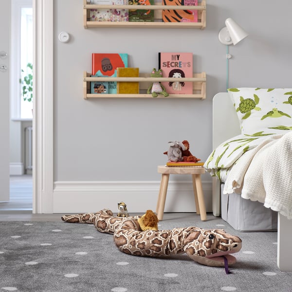 Childs room with tan snake toy, turtle pillow bed, stool, book-filled shelves, grey carpet with white dots.
