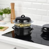 Stove with steaming veggies, pepper, herbs, bowls, cutting board.