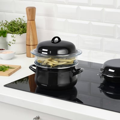 Stove with steaming veggies, pepper, herbs, bowls, cutting board.