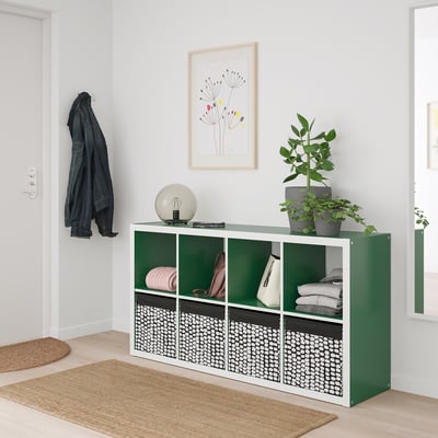 Green DRÖNA box on rug with plant, art, coat.