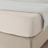 A neatly made bed with a smooth, light-colored fitted sheet, showing elastic edges for comfort and quality.