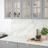 Modern kitchen with light grey cabinets, white marble countertop, avocados, plant, and glassware.