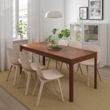 Modern dining set with wooden table, beige chairs, and a bowl of oranges. Large window and hanging light create cozy ambiance.