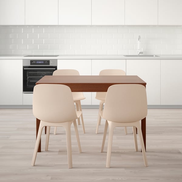 Modern kitchen with wooden table and four beige chairs, positioned against white cabinetry and a built-in oven.
