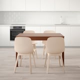 Modern kitchen with wooden table and four beige chairs, positioned against white cabinetry and a built-in oven.