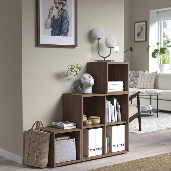 Modern living room with EKET shelf, books, lamp, wicker bag, sofa, chair, and artwork.