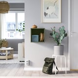 Interior space with green EKET cabinet, cactus, backpack, crane painting, grey walls, wood floors, and large window.