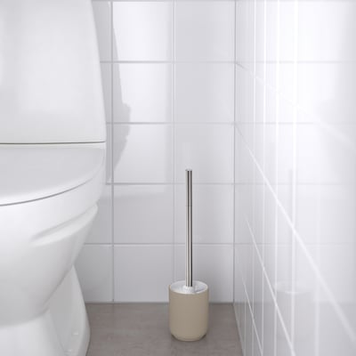 Bathroom with white toilet and beige brush stand holding metallic brush.