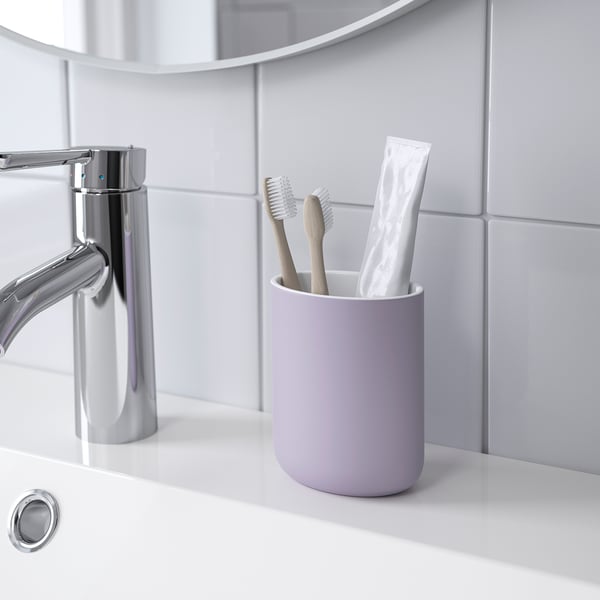 Purple toothbrush holder on bathroom counter, containing toothbrushes and toothpaste.