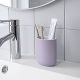 Purple toothbrush holder on bathroom counter, containing toothbrushes and toothpaste.