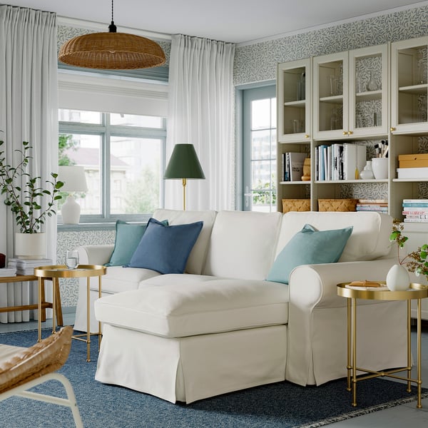 Chic living room with white EKTORP sofa, blue pillows, glass cabinet, green lamp, large window, and patterned rug.