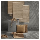 Modern interior decor with beige woven shades, brown pillows on grey blocks, textured grey wall.