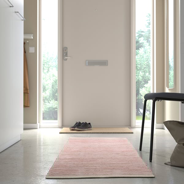 A minimalist entranceway with a small rug on the floor by the door, and another slightly larger rug further in. A stool and a coat hanger are visible.