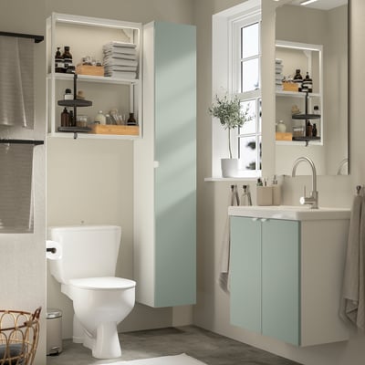 Modern compact bathroom with light turquoise storage, white fixtures, mirror, and greenery by the window.