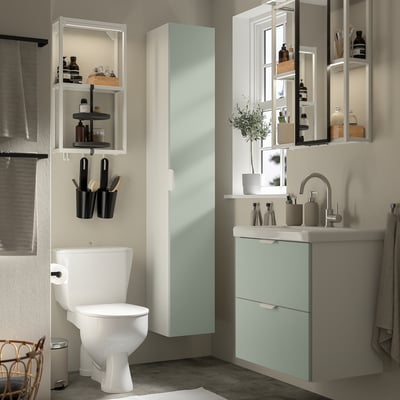 Modern bathroom with ENHET light green cabinet, white toilet, sink, mirror. Open shelves hold toiletries.