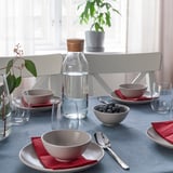 Table set with blue tablecloth, white bowls, clear glasses, red napkins, water jug, and plant, showcasing absorbent fantastik napkins.