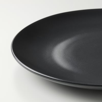 A set of black FÄRGKLAR dinnerware including plates and bowls, made of stoneware with a matte finish, arranged neatly.