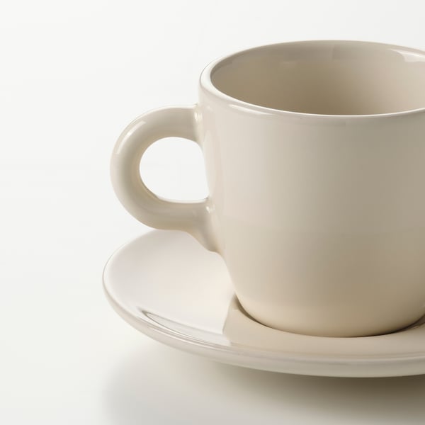 Simple white cup with a smooth handle resting on a matching saucer. High-quality, glossy finish.