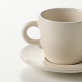 Simple white cup with a smooth handle resting on a matching saucer. High-quality, glossy finish.