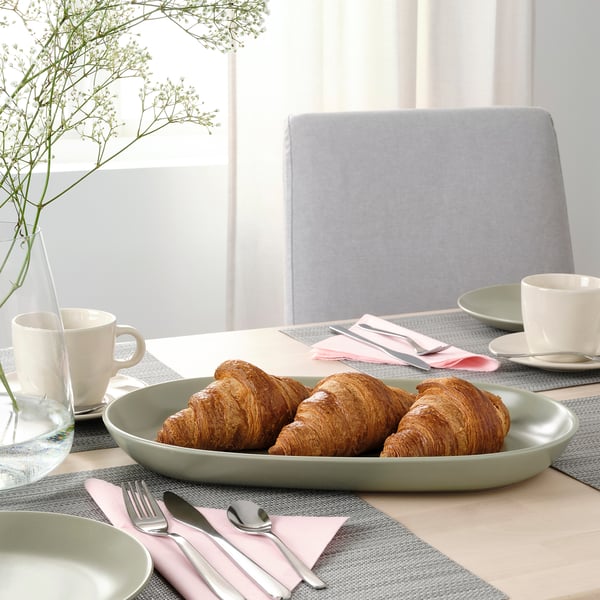 Breakfast setup with croissants on plate, mugs, napkins, and silverware on wooden table.