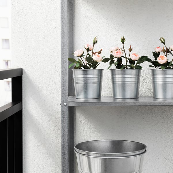 Three potted artificial roses in metal containers on a shelf.