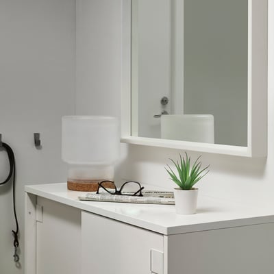 Modern bathroom with white countertop, small white ceramic sink, safety mirror, and tiny FEJKA artificial green plant.