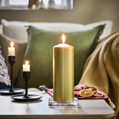 Gold candles on table, one tall, two small. Green pillows, cozy blanket.