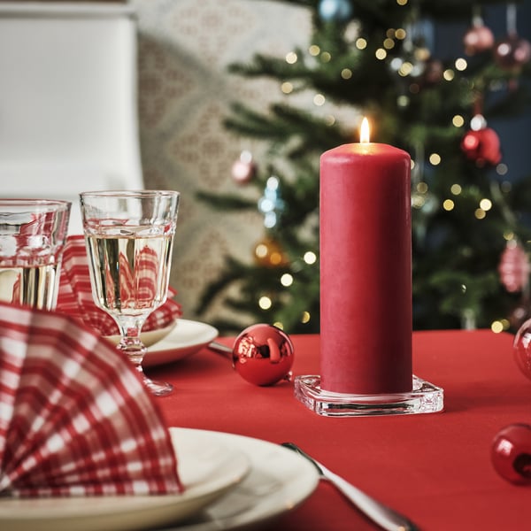 Christmas table set with red candle, glasses, plates, and holiday decorations.