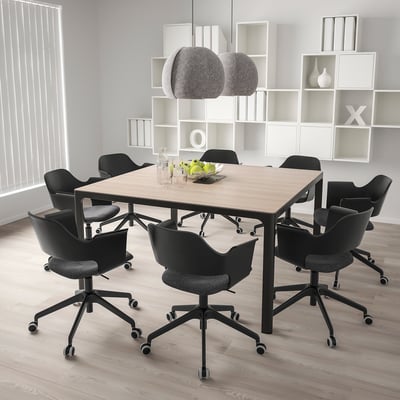 Modern conference table with black chairs, casters, pendant lights, white shelves.