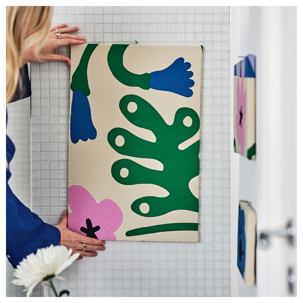 A person hangs a colorful, abstract fabric on tiled wall, likely for decorative or sewing purposes.