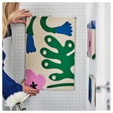 A person hangs a colorful, abstract fabric on tiled wall, likely for decorative or sewing purposes.