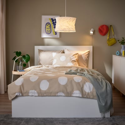 Cozy bedroom with white FJÄLLMIL lamp, elegant bed, green blanket, and plant.